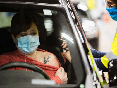 A health worker administers a vaccine to a patient in their vehicle during the first day of mass Moderna COVID-19 vaccinations in Broadbent Arena at the Kentucky State Fair and Exposition Center on January 4, 2021, in Louisville, Kentucky.