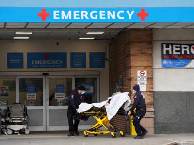 Two paramedics transport a patient through the entrance of an emergency Room