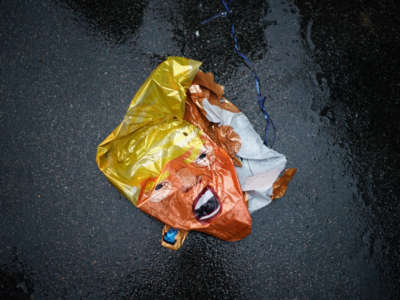 A popped trump balloon lies deflated on the wet asphalt