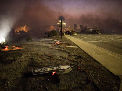 A "One Way" street sign lies on burnt ground as a brush fire surrounds it in Irvine, California, on October 26, 2020.