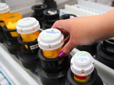 A hand with manicured nails adjusts a perscription bottle