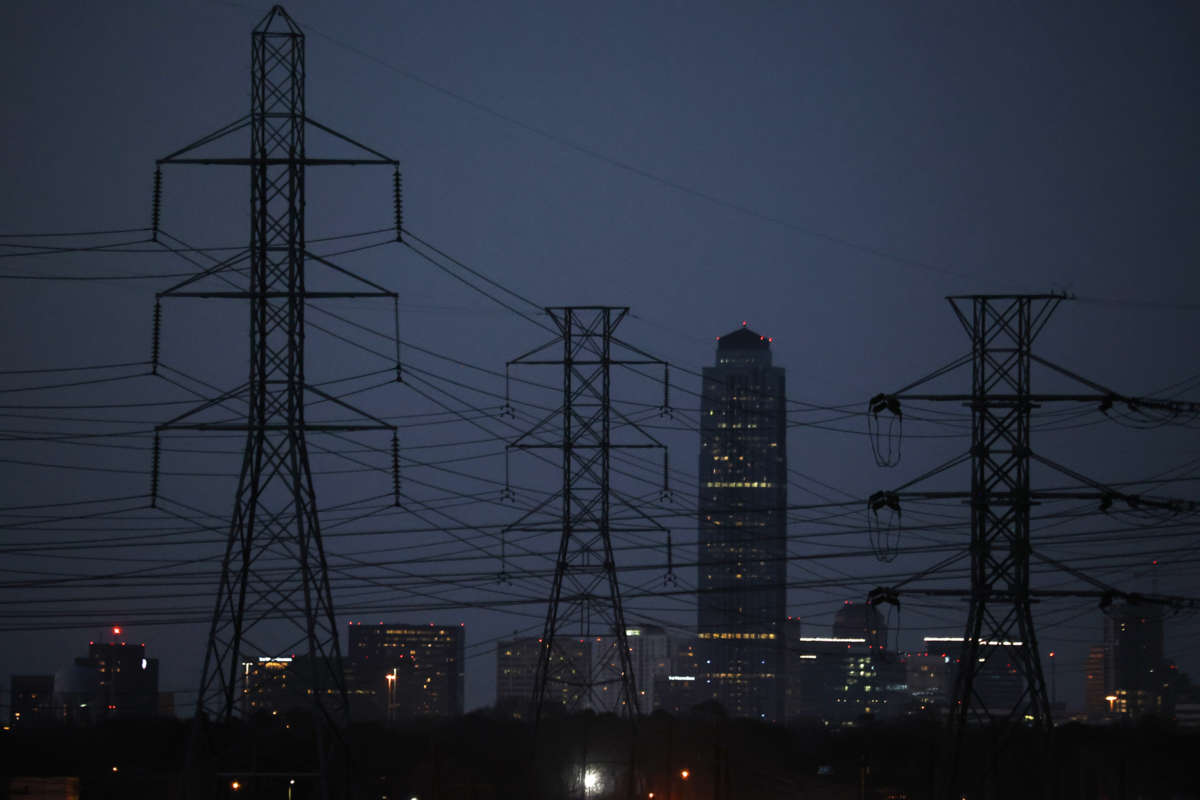 A darkened texas skyline stands behind electrical towers in the foreground