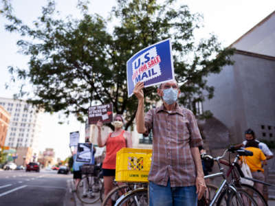 A man holds a sign reading "U.S. MAIL NOT FOR SALE" during a protest