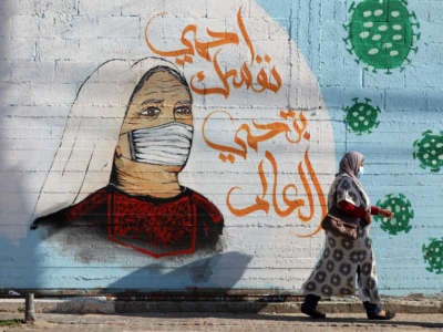 A Palestinian woman, wearing a protective mask amid the COVID-19 pandemic, walks past graffiti with a slogan in Arabic reading: "protect yourself and your family" in Gaza City, on February 27, 2021.