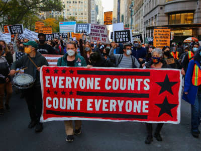 Activists march behind a banner reading "EVERYONE COUNTS, COUNT EVERYONE" during a street protest