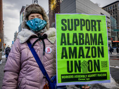 A woman holds a sign reading "SUPPORT ALABAMA AMAZON UNION" during a protest