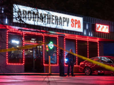 The exterior of a massage parlor at night is surrounded by police tape