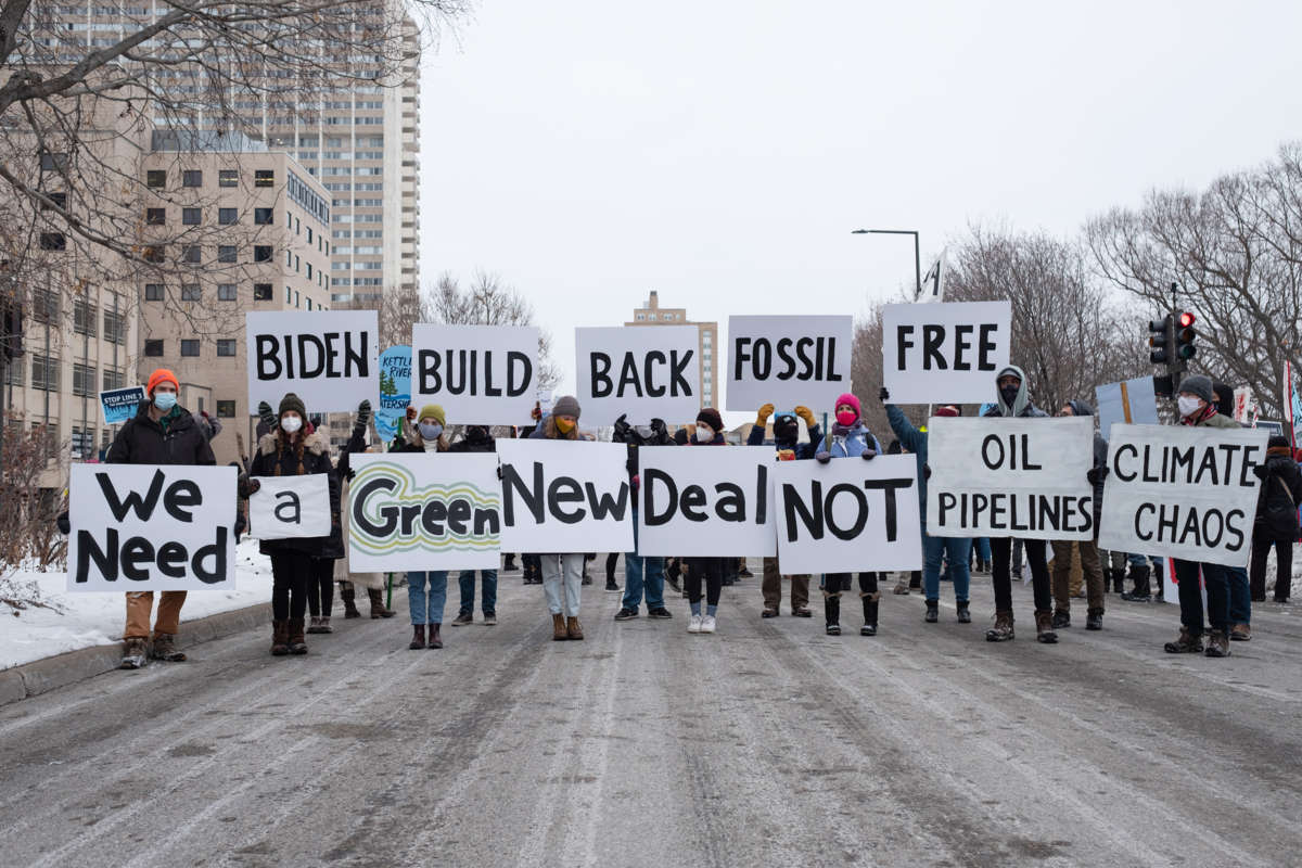 People display signs reading "BIDEN: BUILD BACK FOSSIL FREE, WE NEED A GREEN NEW DEAL NOT OIL PIPELINES CLIMATE CHAOS" during a street demonstration