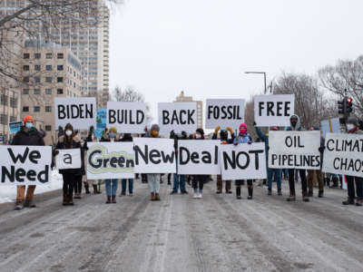 People display signs reading "BIDEN: BUILD BACK FOSSIL FREE, WE NEED A GREEN NEW DEAL NOT OIL PIPELINES CLIMATE CHAOS" during a street demonstration
