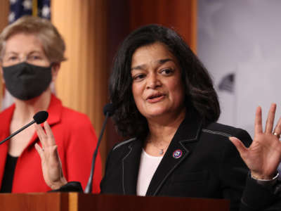 Pramila Jayapal speaks at a podium as Elizabeth Warren stands in the background