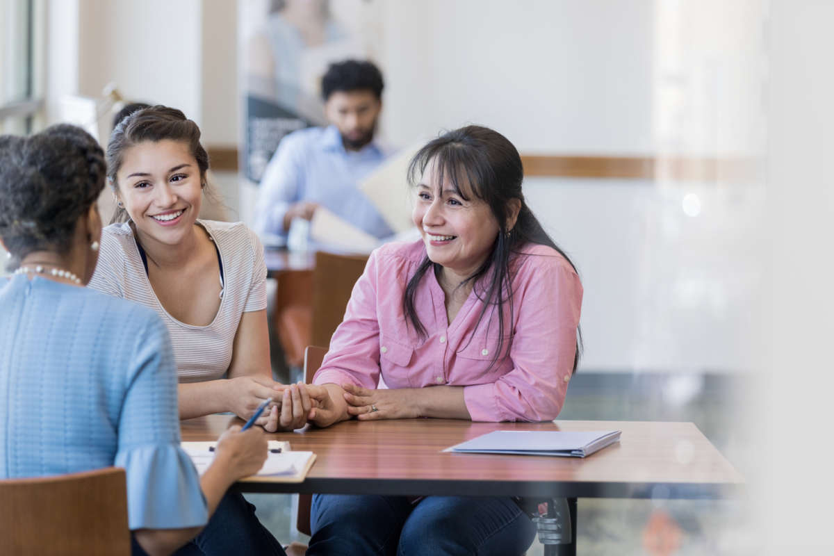 Two women smile as they speak to a bank teller