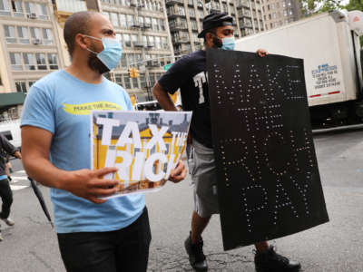 A protester holds a lit sign reading "MAKE THE RICH PAY"