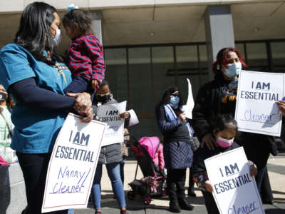 Masked domestic and childcare workers display signs during a protest