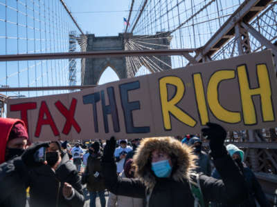Protestors march across the Brooklyn Bridge holding a sign to "tax the rich" to demand funding for excluded workers in the New York State budget on March 5, 2021, in New York City.