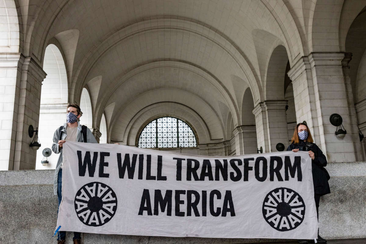 Activists display a banner reading "WE WILL TRANSFORM AMERICA"