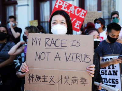 A woman holds a sign reading "MY RACE IS NOT A VIRUS" during a Stop Asian Hate protest