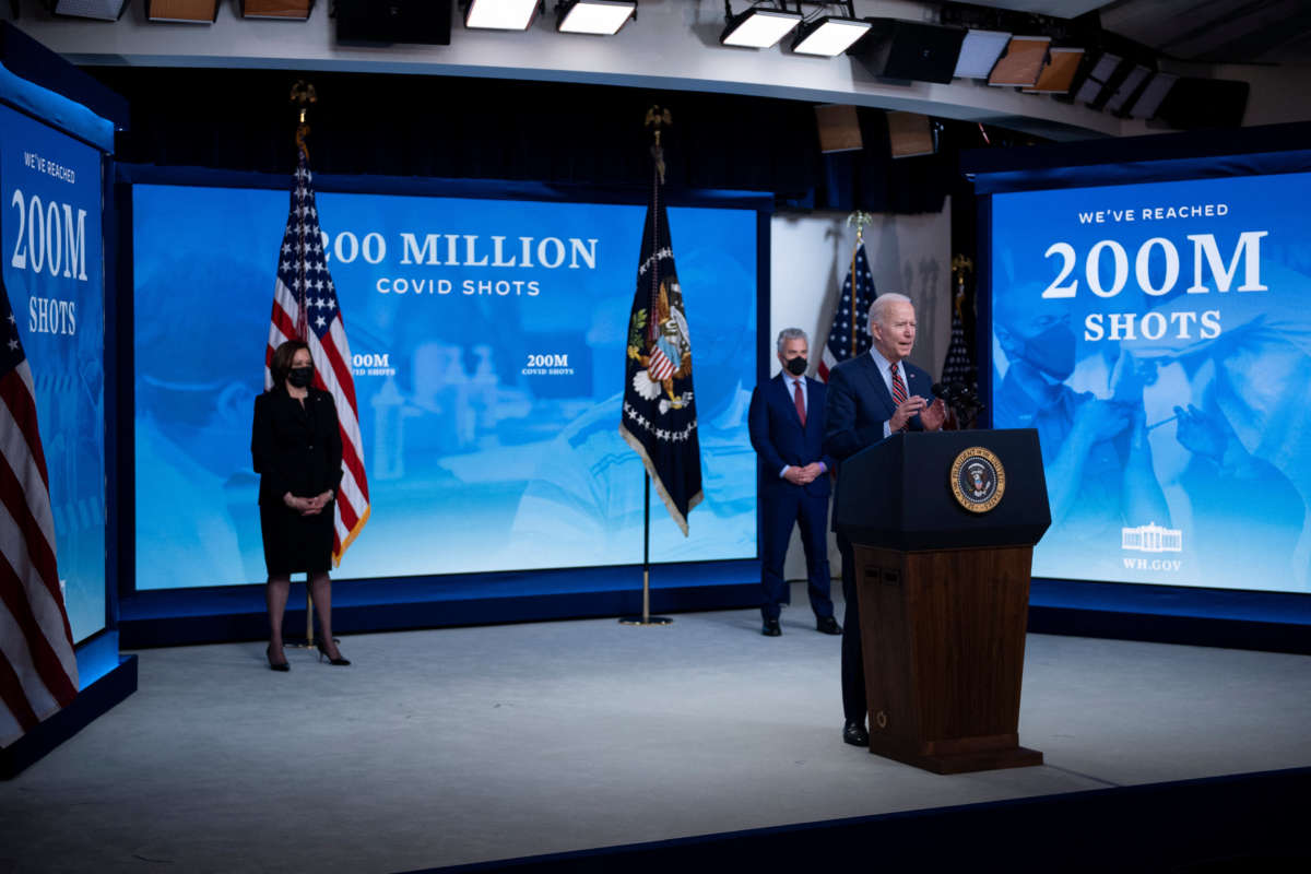 Joe Biden speaks in front of displays that read "WE'VE REACHED 200 MILLION SHOTS"