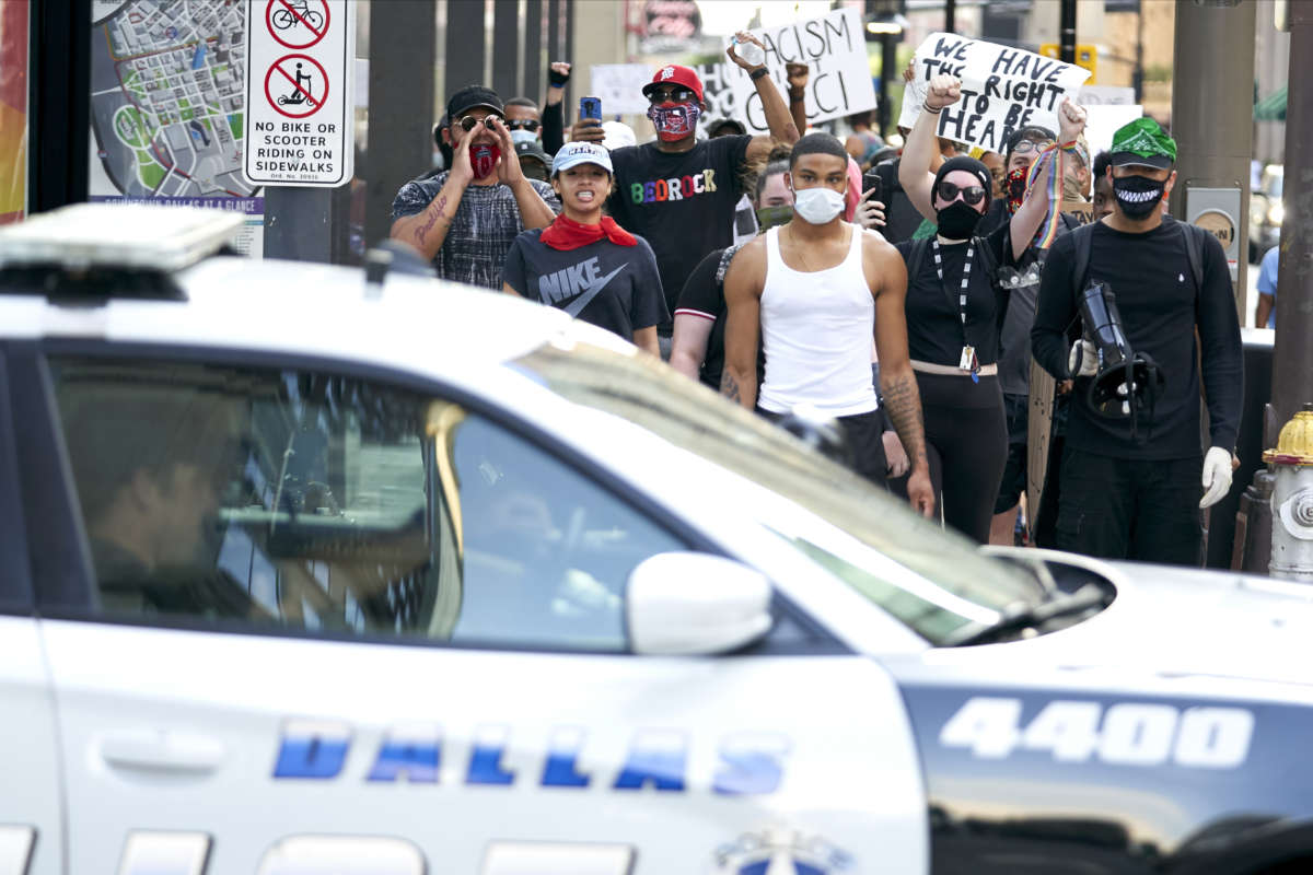Participants in a Black Lives Matter Protest march past a Dallas Police car during a peaceful protest against police brutality and racism on June 6, 2020 in Dallas, Texas.
