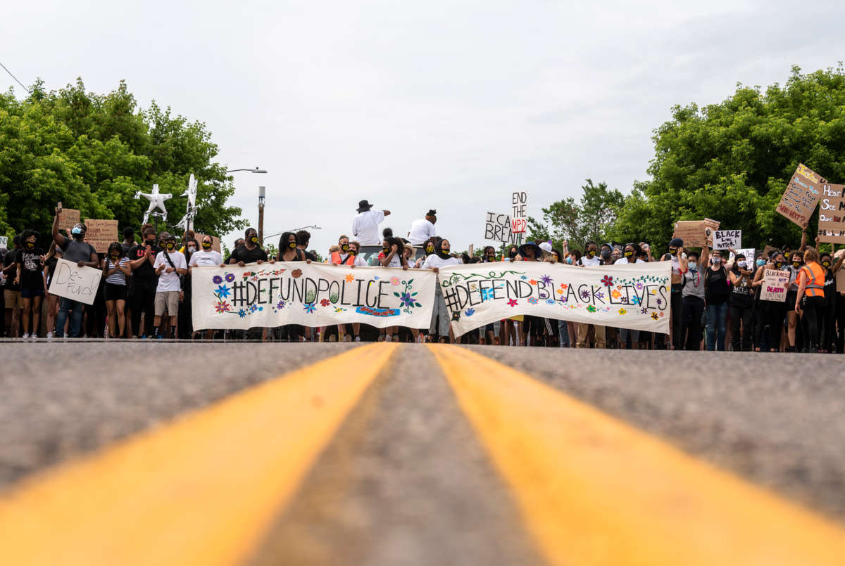 Demonstrators display banners reading "DEFUND THE POLICE" and "#PROTECTBLACKLIVES" during a protest