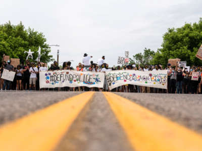 Demonstrators display banners reading "DEFUND THE POLICE" and "#PROTECTBLACKLIVES" during a protest