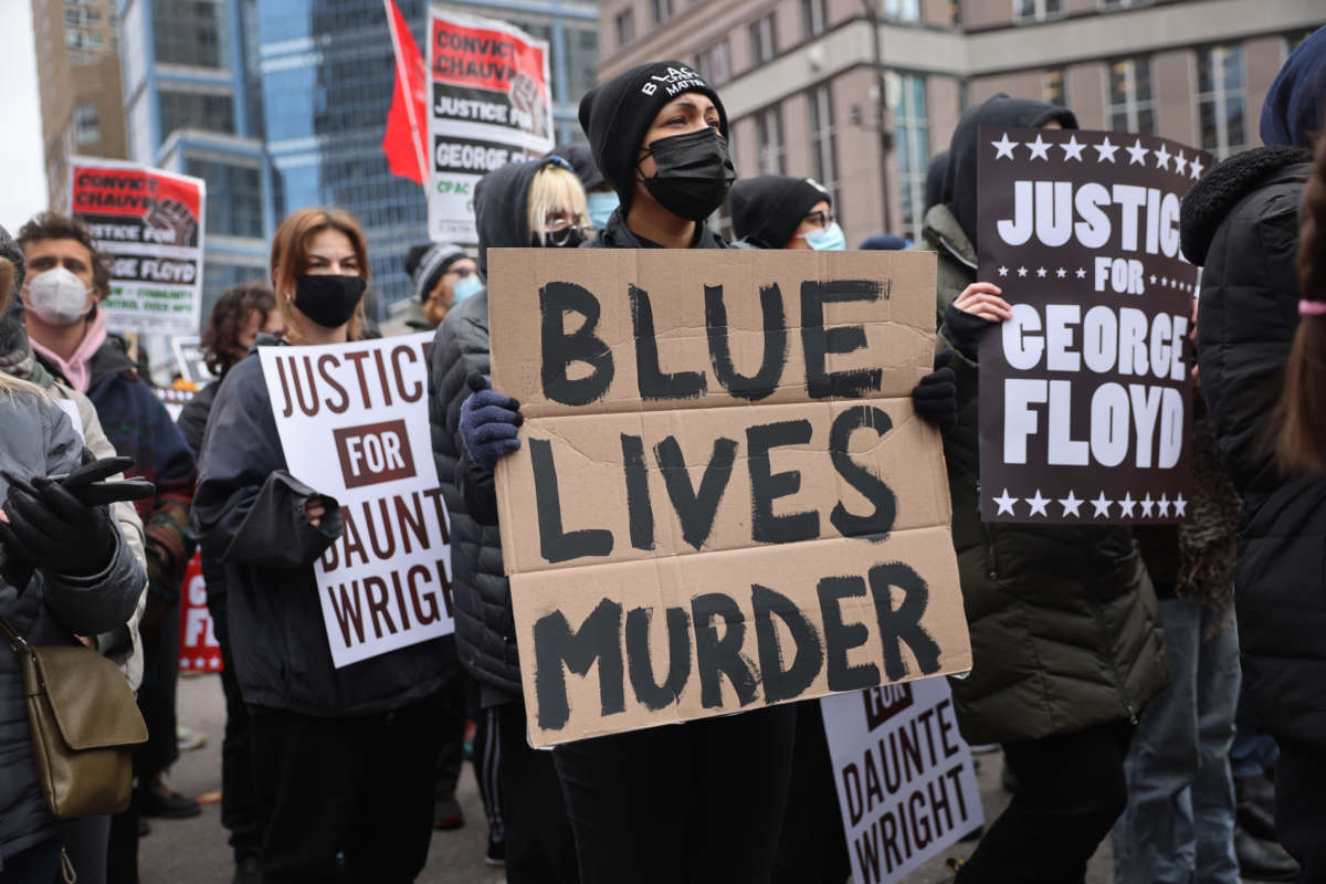 A masked protester holds a sign reading "BLUE LIVES MURDER" during a protest