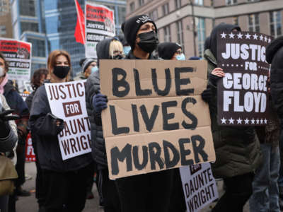 A masked protester holds a sign reading "BLUE LIVES MURDER" during a protest