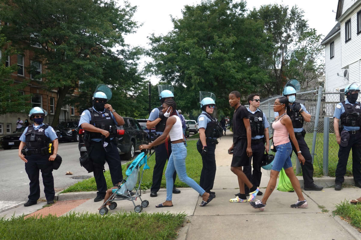 Residents walk past police as they shadow demonstrators protesting police brutality as they march toward downtown on August 15, 2020, in Chicago, Illinois.