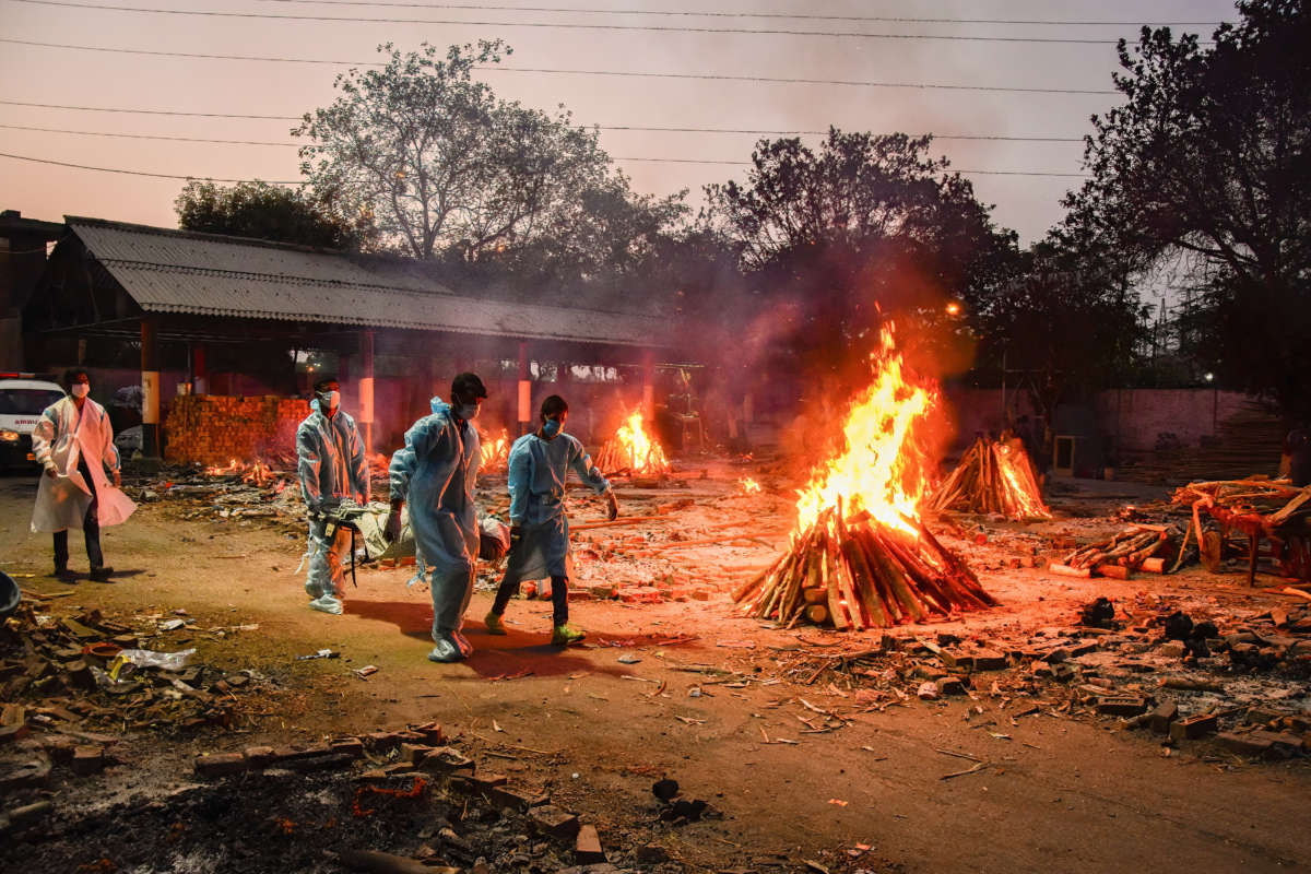 Workers carry the body of a person who has died from COVID-19 as other funeral pyres are seen burning during a mass cremation held at a crematorium in New Delhi, India, on May 3, 2021.