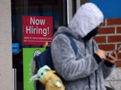A man wearing a face mask stands next to a "Now Hiring" sign in front of a store on December 18, 2020, in Arlington, Virginia.