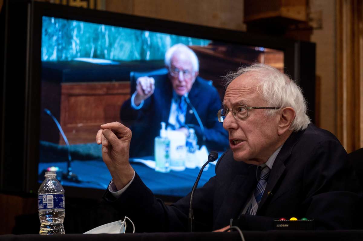 Bernie Sanders speaks in front of a large screen showing Bernie Sanders speaking