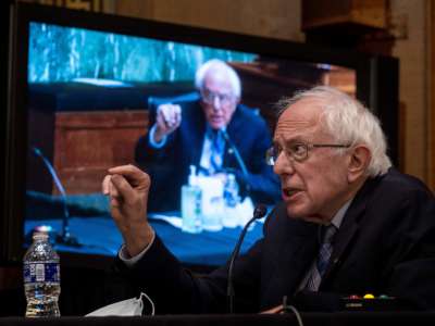 Bernie Sanders speaks in front of a large screen showing Bernie Sanders speaking