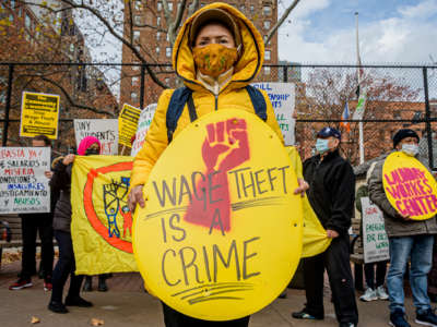 A protester holds a sign reading "WAGE THEFT IS A CRIME"