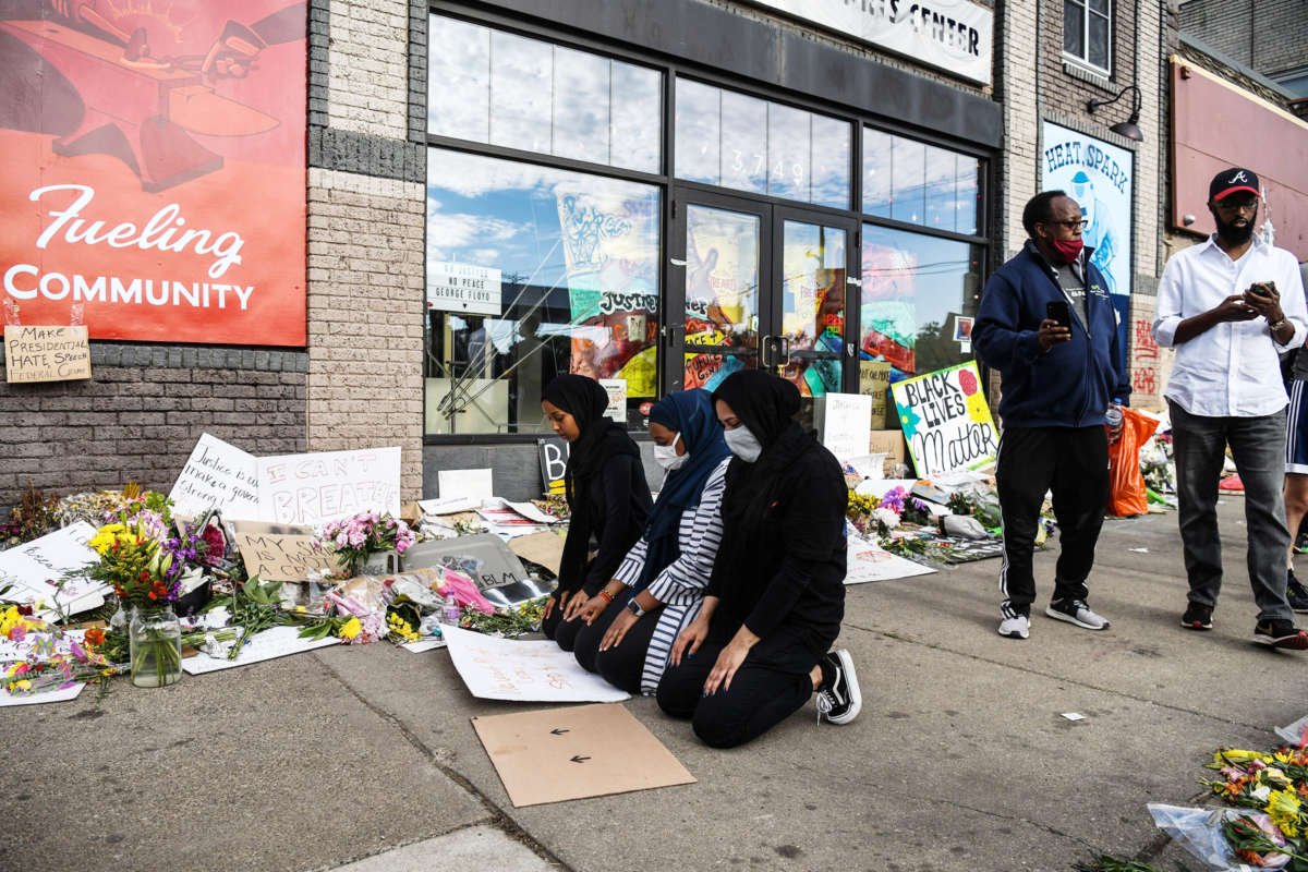 Three young Muslim women pray at the site of George Floyd's murder