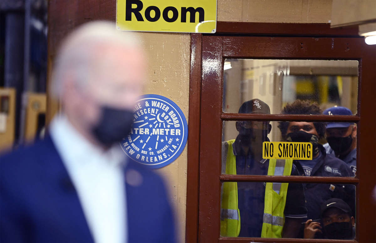 Three workers watch Joe Biden from behind a closed door