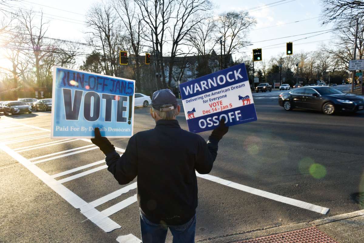 An elderly volunteer holds two signs encouraging people to vote