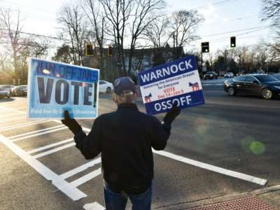 An elderly volunteer holds two signs encouraging people to vote