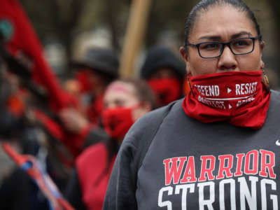 An Indigenous activist with perfect eyebrows looks onward as other activists demonstrate behind her