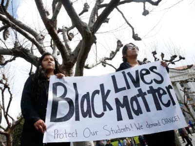 Two students display a sign reading "BLACK LIVES MATTER" beneath a leafless tree