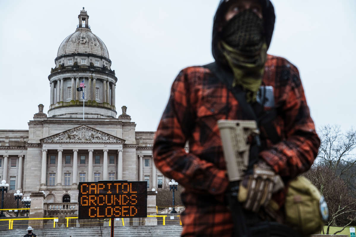 An armed goofball stands alone in front of a closed capitol building