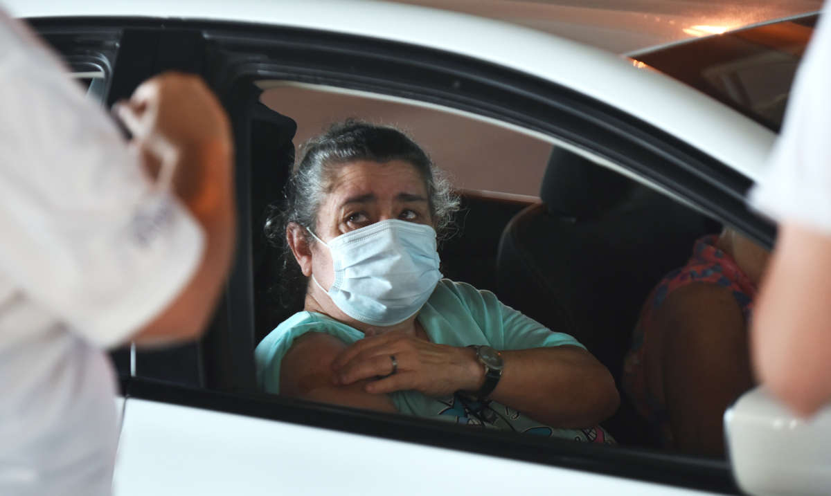 A masked woman pulls up her sleeve to receive the covid-19 vaccine through her car window