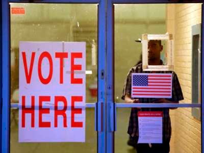 A man stands partially obscured behind sineage denoting the entrance of a U.S. polling place