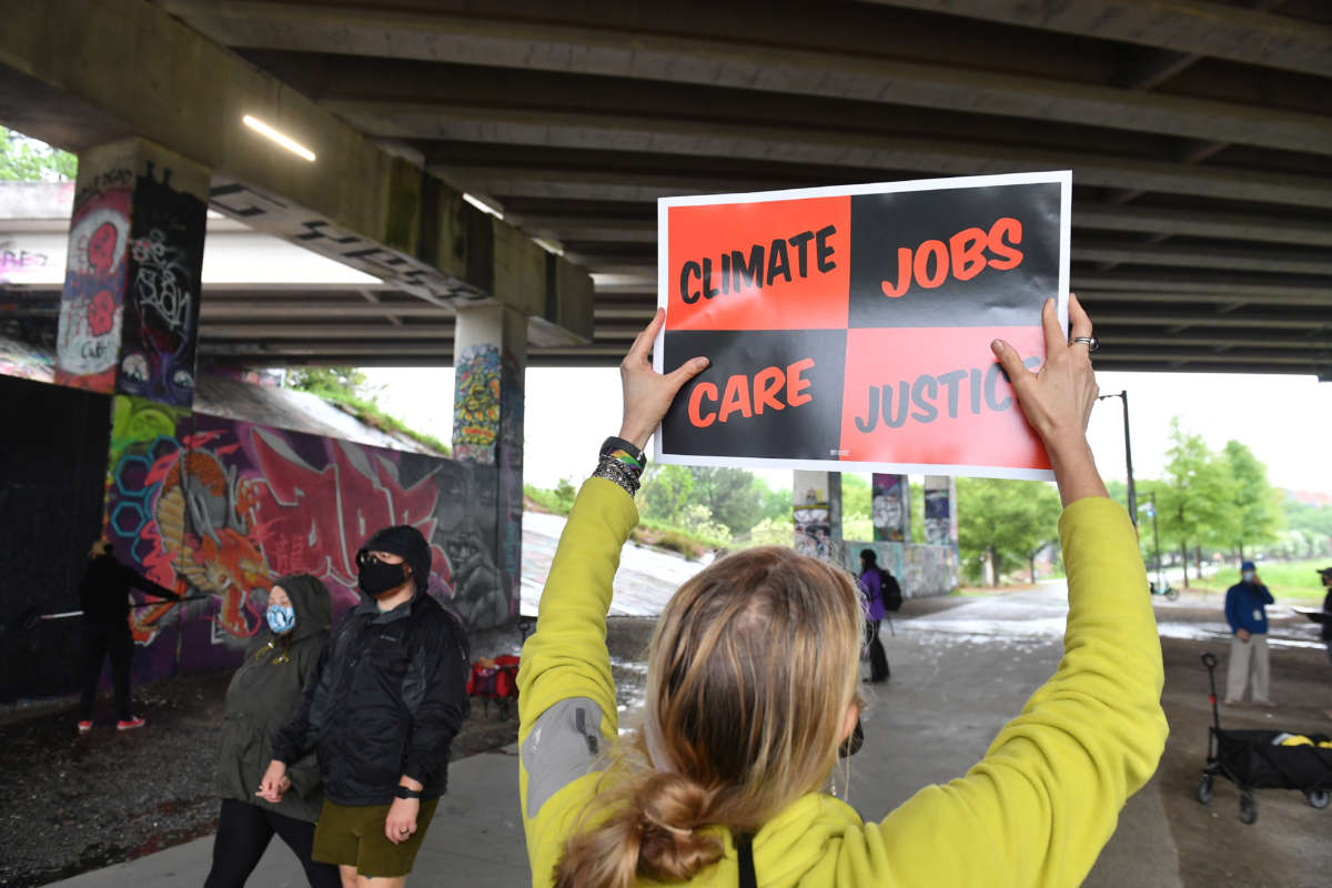 A person holds a sign reading "CLIMATE, JOBS, CARE, JUSTICE" under an overpass