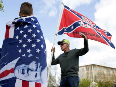 Keith Weber of Centralia, Washington, holds a flag that combines a Gadsden flag from the American Revolution with a Confederate flag from the U.S. Civil War as he talks to protesters holding flags with then-President Donald Trump on them as people demonstrate against Washington State's stay-home order at the state capitol in Olympia, Washington, on April 19, 2020.