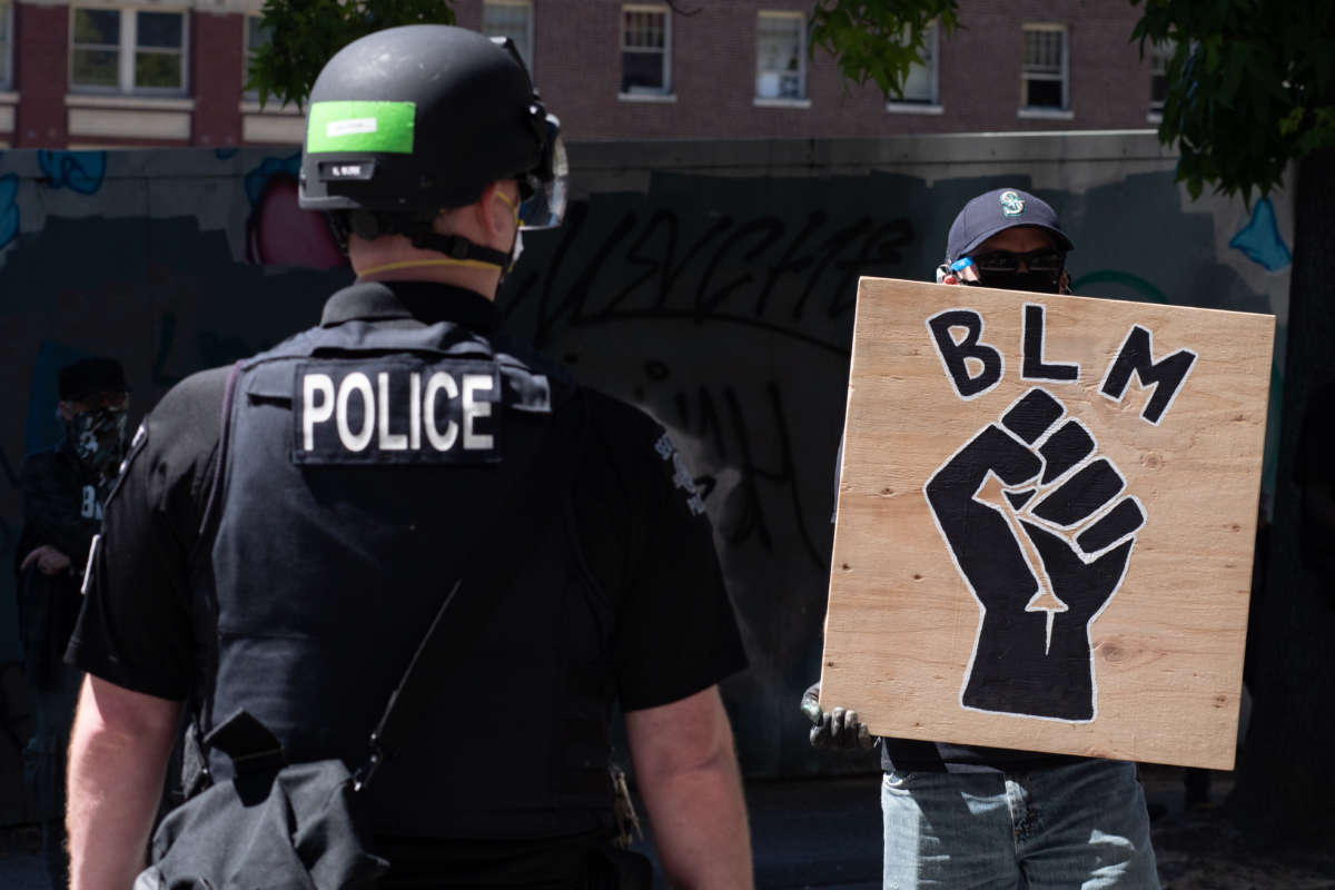 A police officer stands in front of a Black Lives Matter sign in Seattle, Washington, on August 9, 2020. In one case found by ProPublica, a Seattle Police Department officer who struck a protester "six to eight punches over six seconds" received a written reprimand.