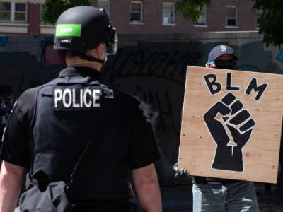 A police officer stands in front of a Black Lives Matter sign in Seattle, Washington, on August 9, 2020. In one case found by ProPublica, a Seattle Police Department officer who struck a protester "six to eight punches over six seconds" received a written reprimand.