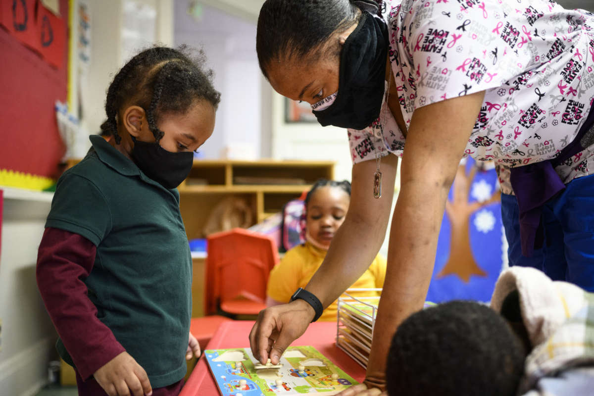 Shanikia Johnson, a teacher, helps a three-year-old clean up a puzzle at Little Flowers Early Childhood and Development Center in the Sandtown-Winchester neighborhood of Baltimore, Maryland, on January 12, 2021.