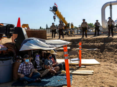 Environmental activists conduct a sit-in in front of the construction equipment as police in riot gear line up at the Line 3 pipeline pumping station near the Itasca State Park, Minnesota, on June 7, 2021.