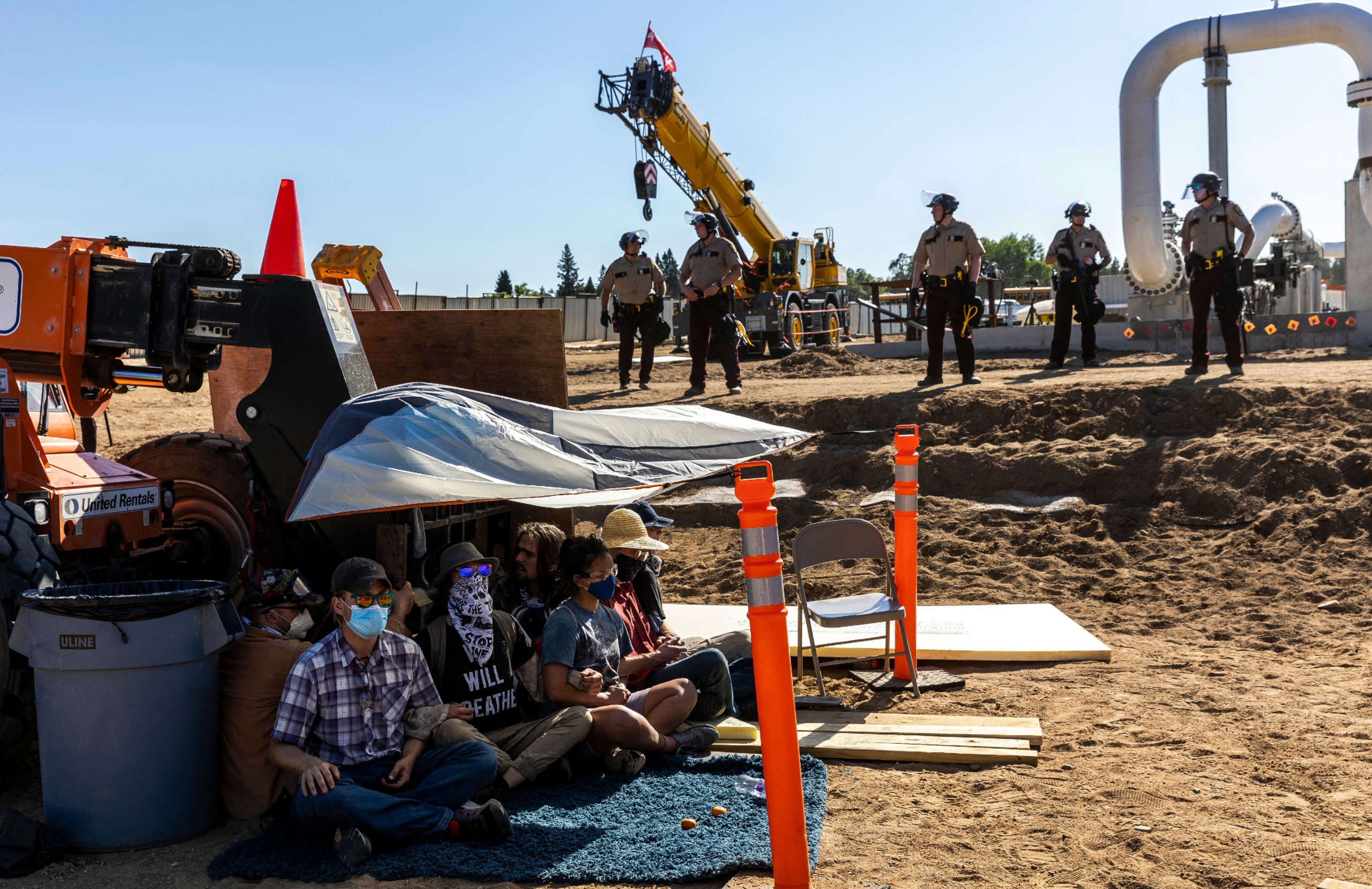 Environmental activists conduct a sit-in in front of the construction equipment as police in riot gear line up at the Line 3 pipeline pumping station near the Itasca State Park, Minnesota, on June 7, 2021.