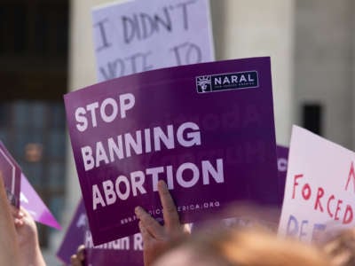 A protester holds a purple sign reading "STOP BANNING ABORTION" during a protest