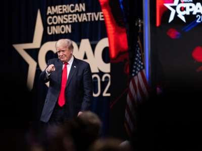 Donald Trump points at his fans in front of a large banner reading "CPAC"